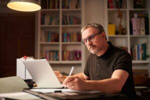 Man sitting at a table holding a pen and computer